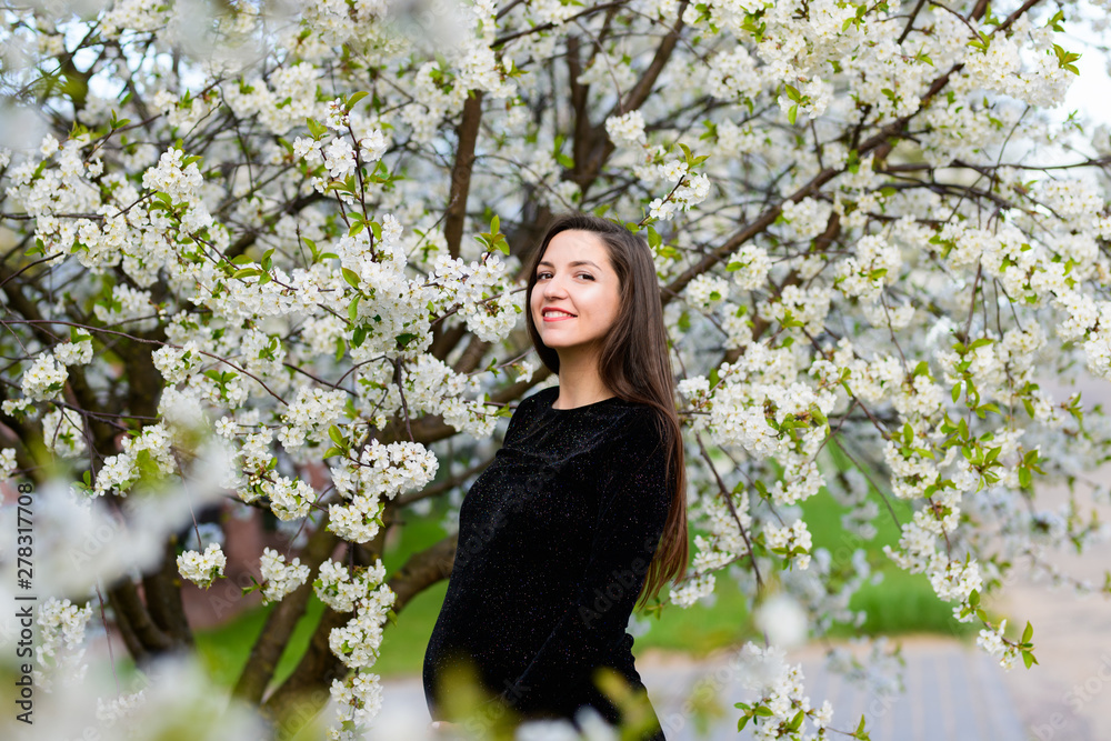 Pregnant girl in the flowered garden. beautiful pregnant girl in a black dress is standing in a flowered garden Pregnant girl in the flowered garden. beautiful pregnant girl in a black dress is standing in a flowered garden