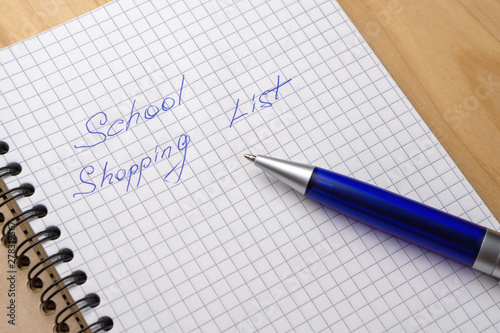 Blue pen on a notebook with sheets in a cage. Sign - school shopping list