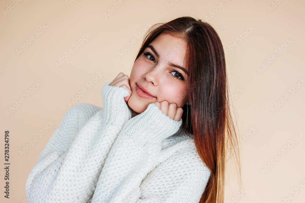 Portrait of beautiful smiling teenager girl with clean skin and dark long hair in cozy white sweater on beige background Portrait of beautiful smiling teenager girl with clean skin and dark long hair in cozy white sweater on beige background