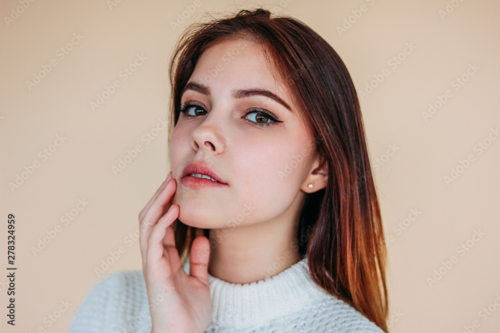 Beautiful smiling girl with clean skin and dark long hair in cozy white sweater on beige background Beautiful smiling girl with clean skin and dark long hair in cozy white sweater on beige background