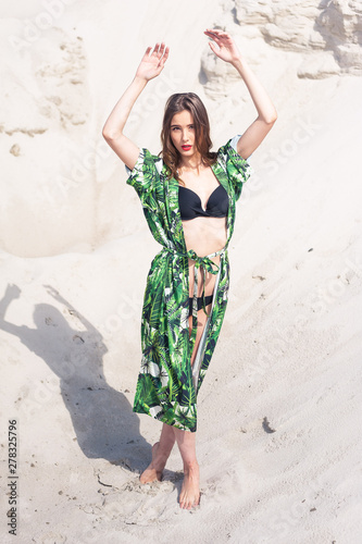 Beautiful young woman walking on the beach, green desert wear.