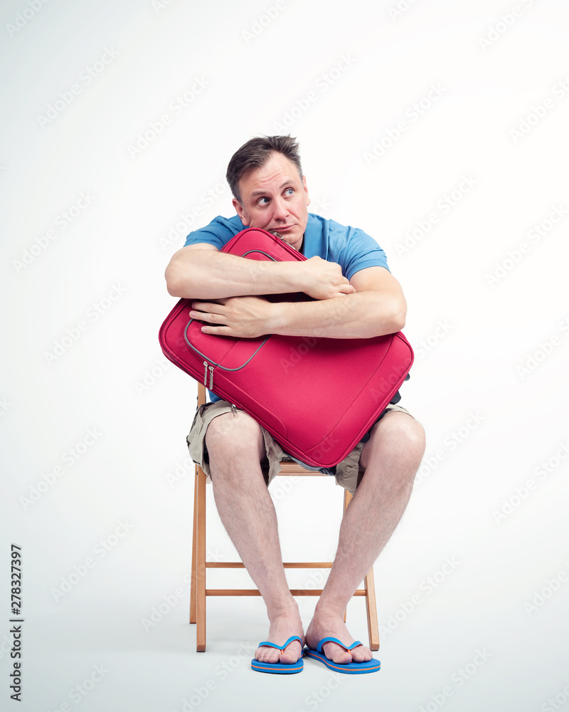 Man in shorts and a t-shirt with a red suitcase sits on a chair waiting Man in shorts and a t-shirt with a red suitcase sits on a chair waiting