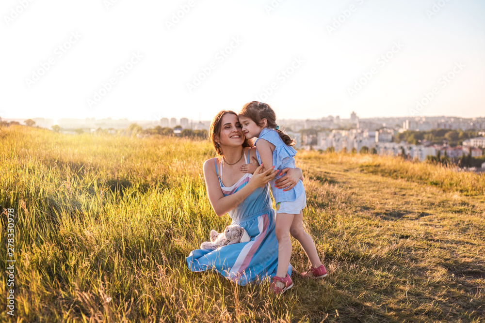 Young mother and daughter, hugging and playing in a golden field of sunshine. Young mother and daughter, hugging and playing in a golden field of sunshine.