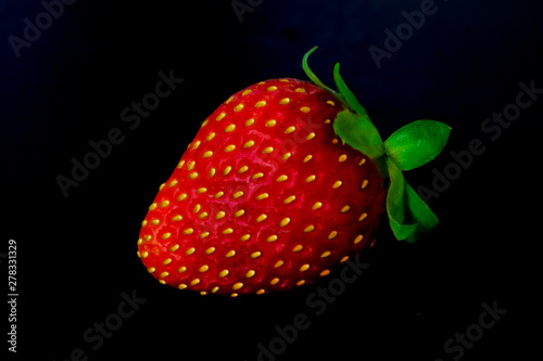 Ripe red strawberries with yellow seeds and a green tail on a black background close-up.
