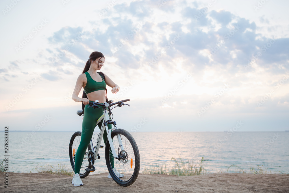 Portrait of a beautiful young brunette woman with a backpack checking pulse after bicycle ride at sunrise. Portrait of a beautiful young brunette woman with a backpack checking pulse after bicycle ride at sunrise.