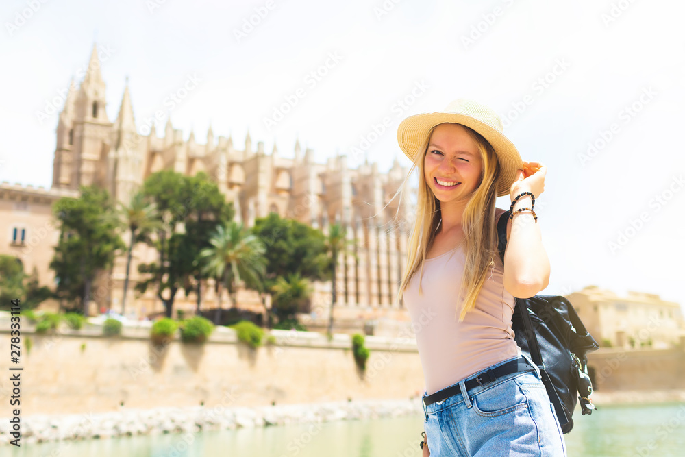 Summer hot vacation Europe Spain holiday travel tourism architecture - young beautiful Caucasian walking smiling attractive young girl with hat and backpack in front of the city castle in the city