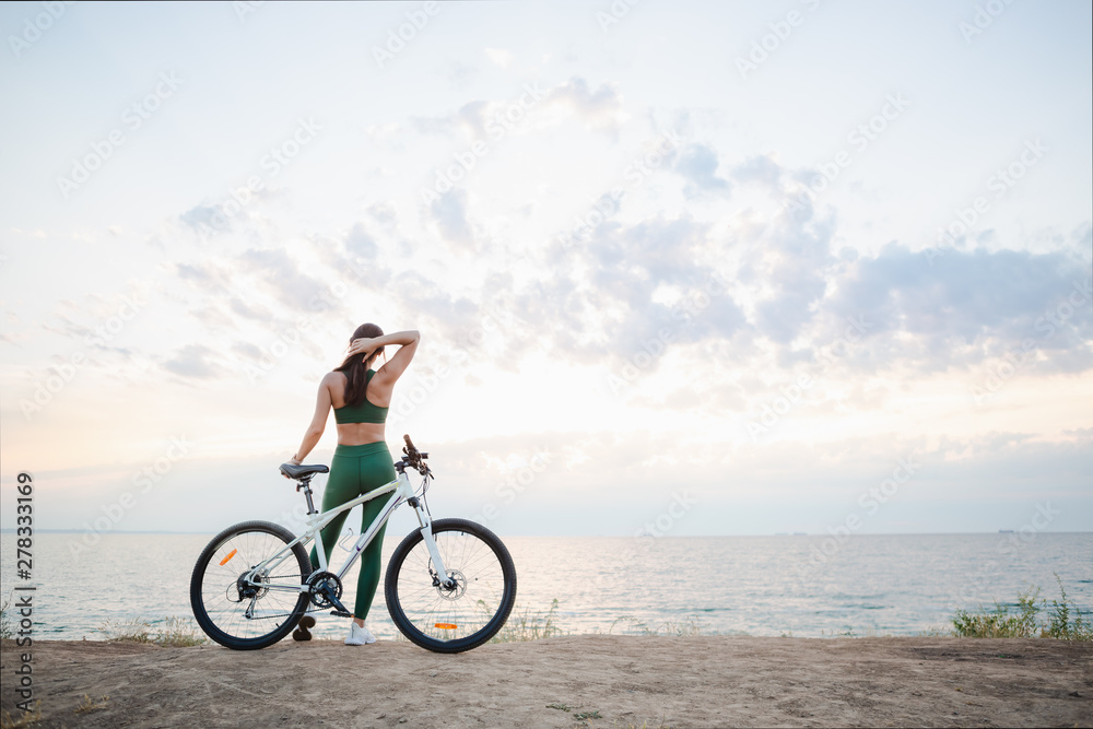 Young brunette woman on a bicycle at sunrise.