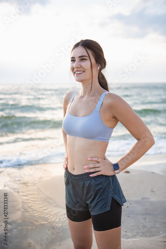 Pretty brunette woman resting after workout at the sea shore at sunrise listening to the music.
