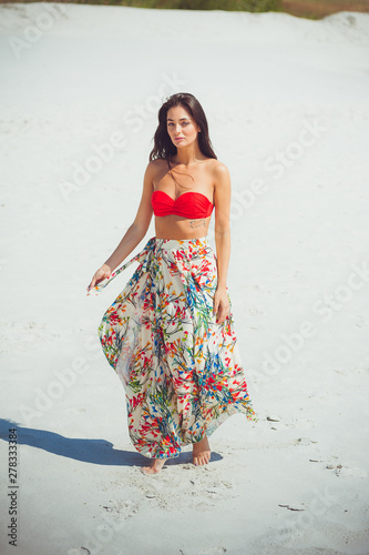 A beautiful woman dressed in beach clothes gracefully walks in the desert in the sand