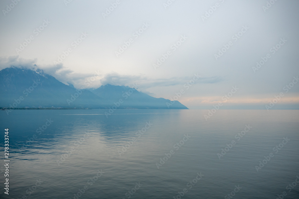 Beautiful view of Geneva lake with small boat on cloudy sky and alpine mountain background with copy space