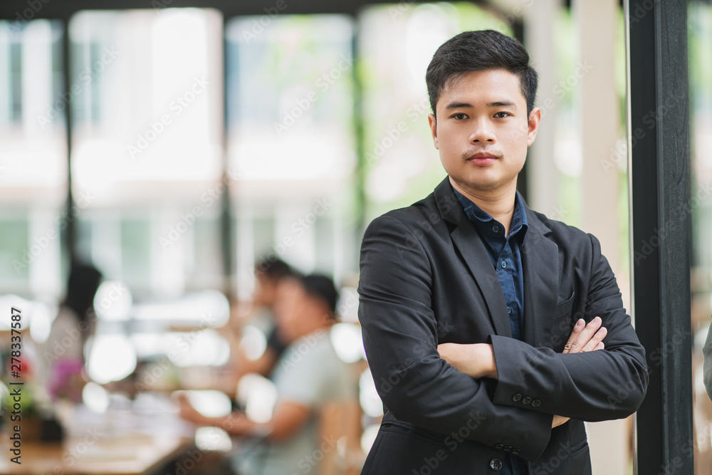Portrait of smiling young business man with arm crossed on office background and looking at camera Portrait of smiling young business man with arm crossed on office background and looking at camera