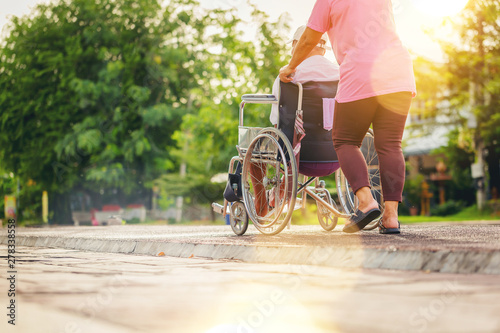 Disabled mature senior man in a wheelchair relaxing in a park by his wife take care with sunset background