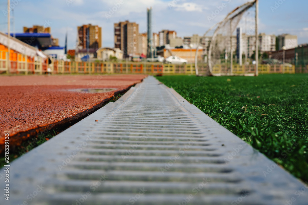 jogging track with metal grating and green grass.