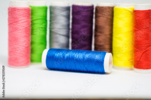 Multi-colored spools of cotton threads for sewing on a white background close-up