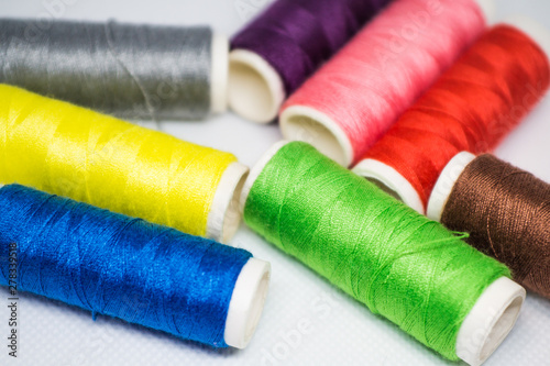 Multi-colored spools of cotton threads for sewing on a white background close-up
