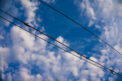  Electric wires leading to the house against the blue sky with white clouds