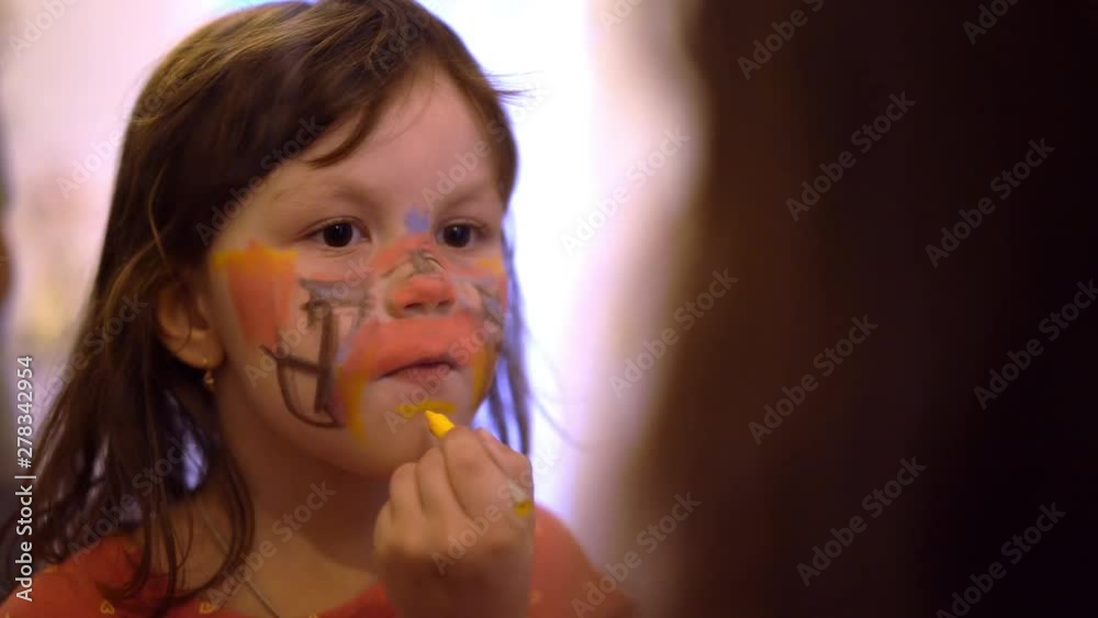 Pportrait of little caucasian girl paints on face with face paint in front the mirror Pportrait of little caucasian girl paints on face with face paint in front the mirror