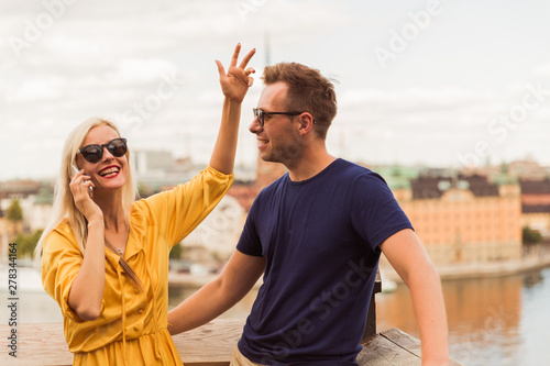 Portrait of the cheerful young couple who is standing against the background of the city and river and a woman speaking by phone