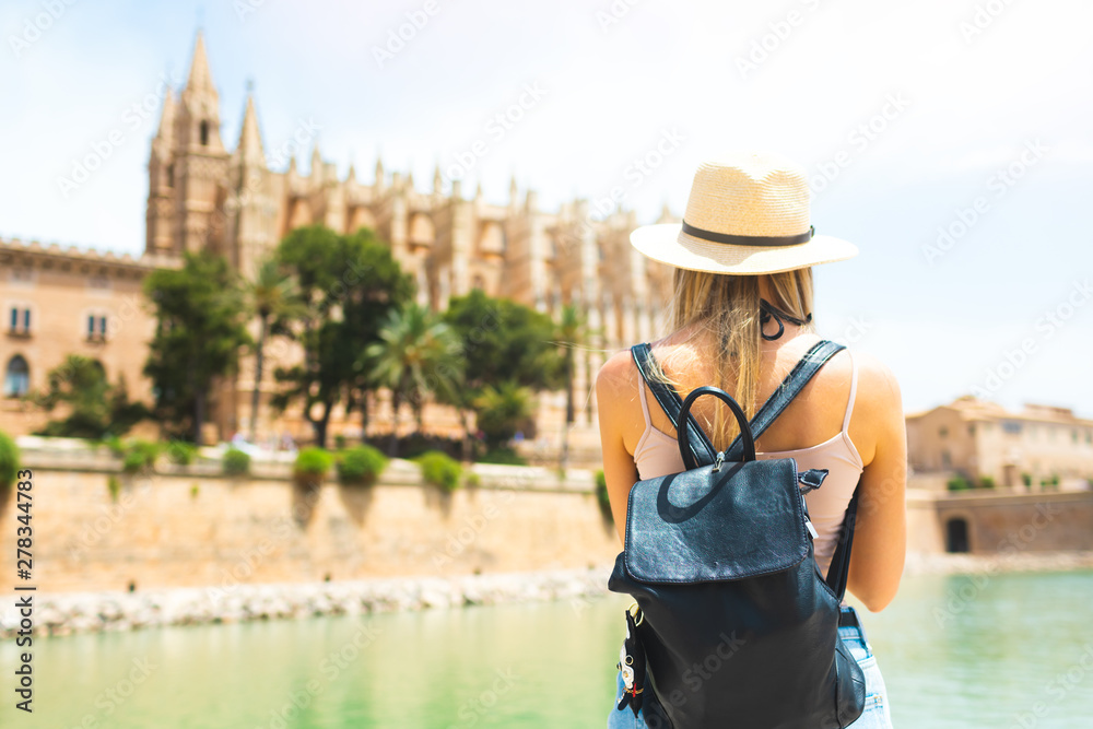 Summer hot vacation Europe Spain Mallorca Palma holiday travel tourism architecture - young beautiful Caucasian walking  attractive young girl with hat and backpack in front of the city castle