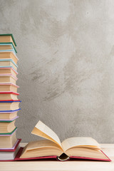 Education and reading concept - group of colorful books on the wooden table, concrete wall blackboard