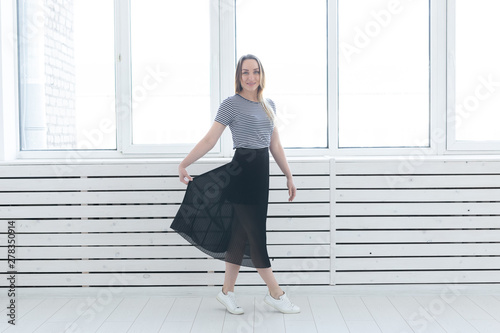 Youth, style and people concept - young woman on black skirt and sneakers standing near the window © satura_