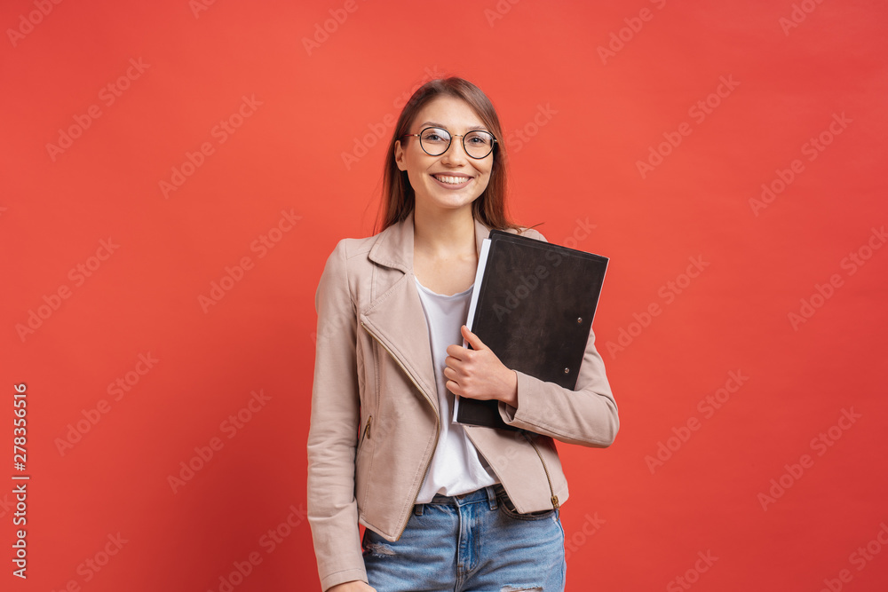 Young smiling student or intern in eyeglasses standing with a folder on red background. Young smiling student or intern in eyeglasses standing with a folder on red background.
