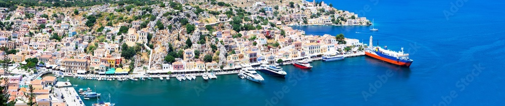 Panoramic view of beautiful bay with colorful houses on the hillside of Symi island in Greece. View on Greek sea Symi island harbor with ships, yachts and houses on island hills
