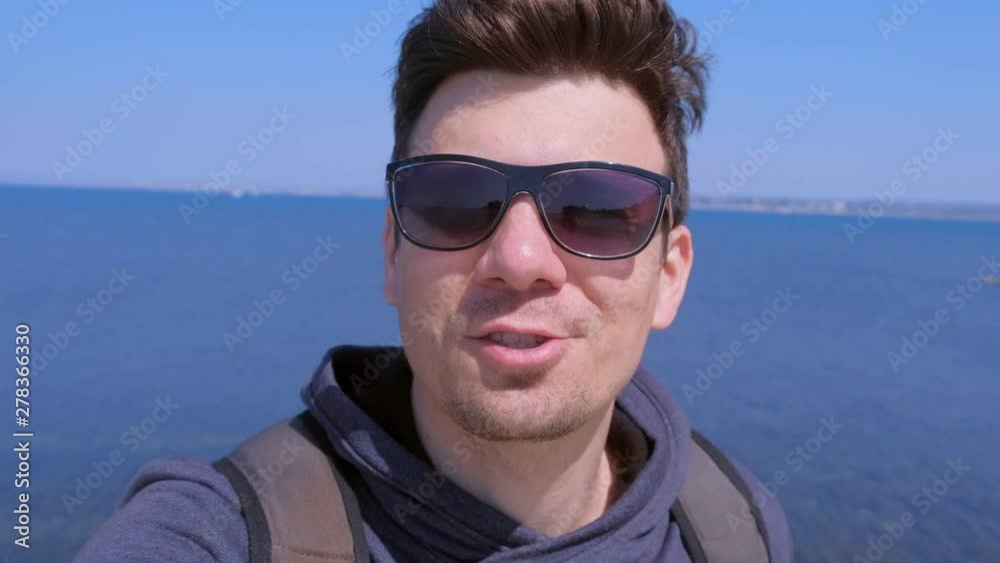 Portrait of young guy on sea background. Man blogger traveller selfie camera talks about vacation at sea. Young tourist smiles and shares his impressions about rest at sea. Travel journey concept.