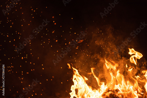 Burning red hot sparks fly from big fire. Beautiful abstract background on the theme of fire. Burning coals, flaming particles flying off against black background.