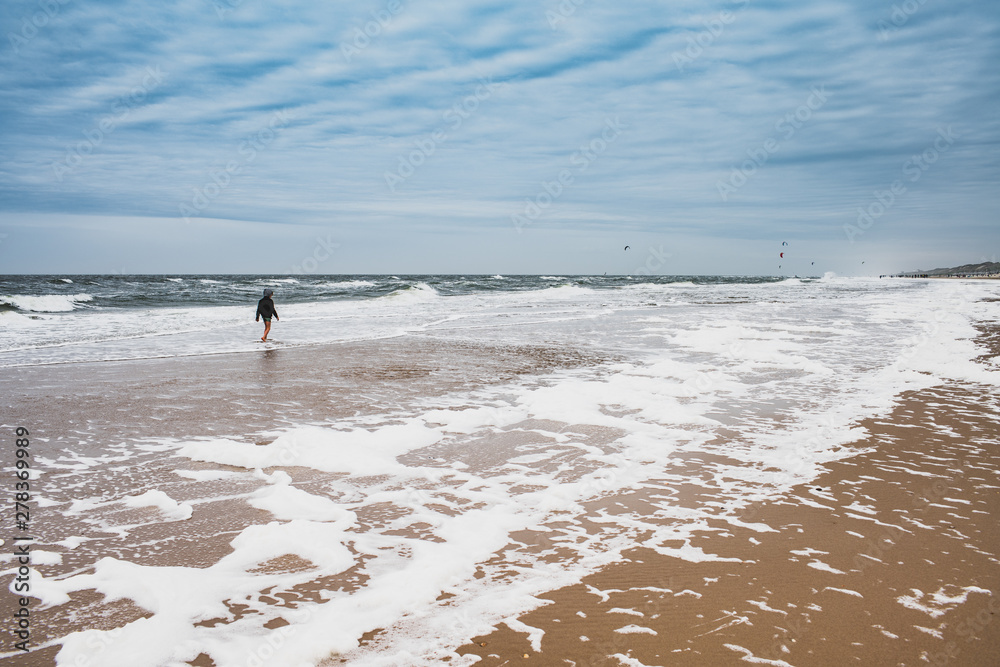 Little boy walking along a beach at North-Sea of Netherlands coast alone.