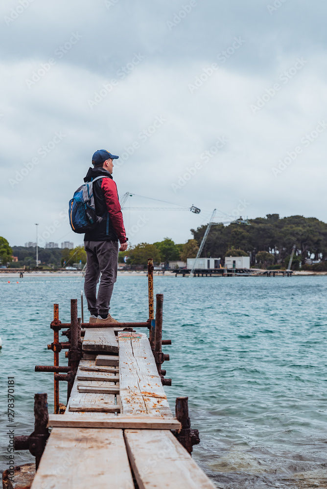 Fototapeta premium man standing at edge of the small fishing pier looking at stormy sea