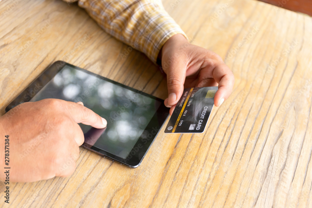The male hand caught the credit card and was doing business on the internet in the tablet on the wooden table. The male hand caught the credit card and was doing business on the internet in the tablet on the wooden table.