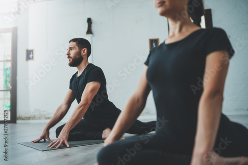 Fototapeta Naklejka Na Ścianę i Meble -  Yoga Practice Exercise Class Concept. Two beautiful people doing exercises.Young woman and man practicing yoga indoors