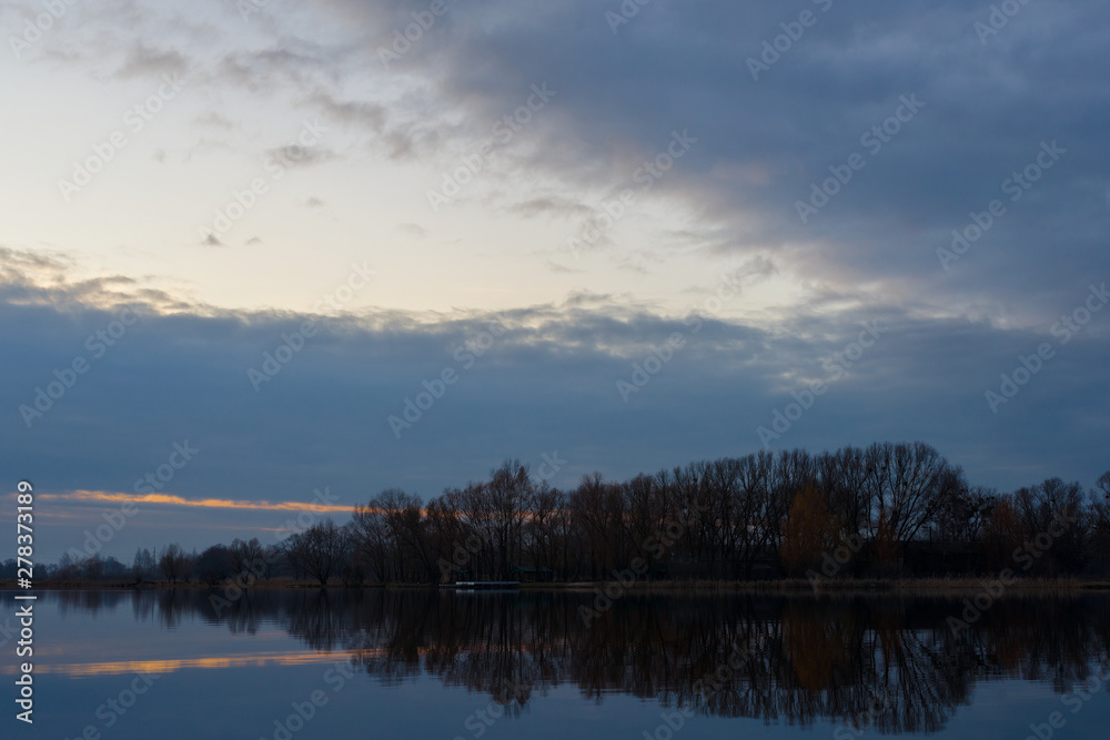 Gray evening sunset above the lake or river. Blue clouds on horizon