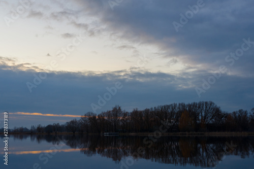 Gray evening sunset above the lake or river. Blue clouds on horizon