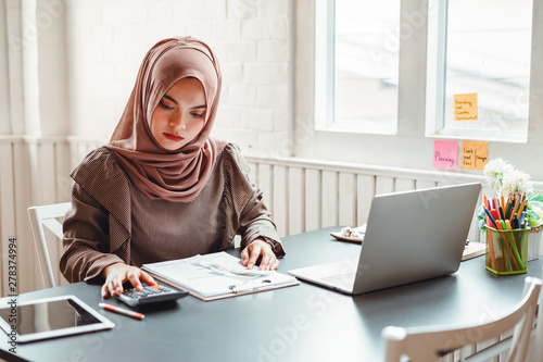 Happy beautiful muslim business woman brown hijab working about financial with business report and calculator in home office.
