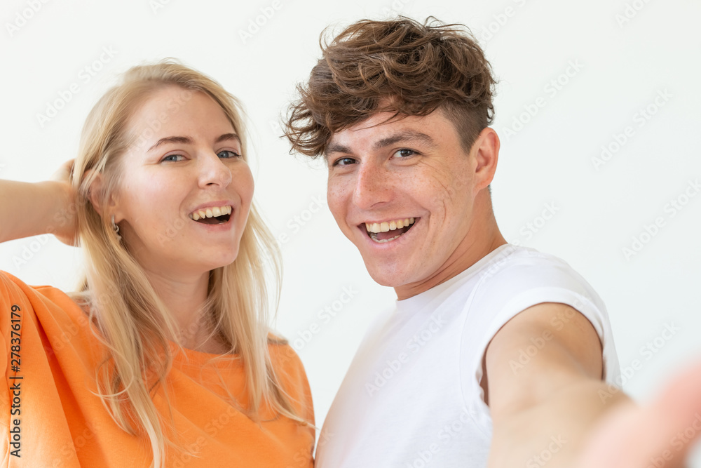 Charming young couple cute blond girl girl take a selfie posing over white background. Concept a young couple of teenagers or millennials In love. Charming young couple cute blond girl girl take a selfie posing over white background. Concept a young couple of teenagers or millennials In love.