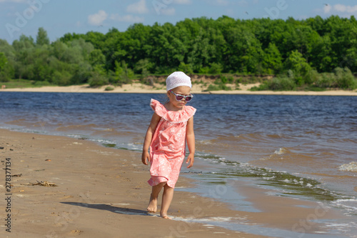 Little girl walking on the summer beach washed by waves with beautiful landscape on background