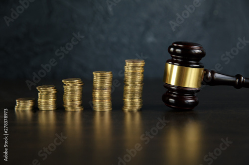 Close-up Of A Judge's Hand Holding Gavel Over Stacked Golden Coins