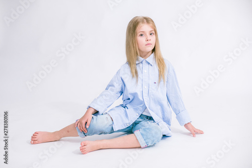 Beautiful fashionable little girl with blond hair in jeans clothes on a white background in studio