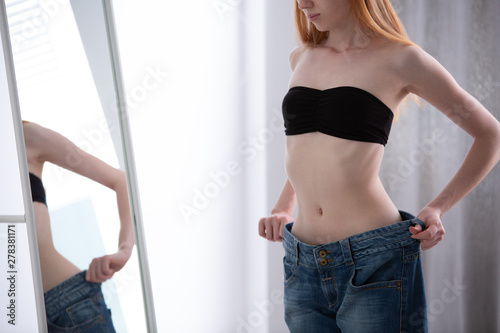 Girl looking at herself in a mirror wearing too big trousers