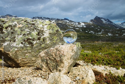 Tilted view of glass orb on rock reflection a mountain range photo