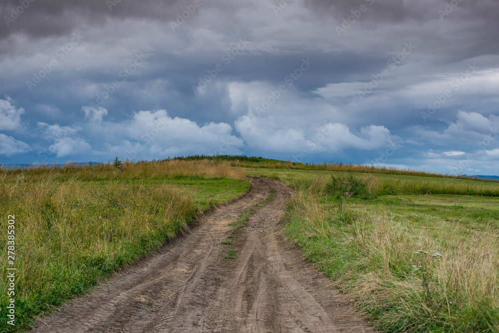 Dirt road leading to the top of the hill, dramatic storm clouds at summertime in Transylvania, Romania.