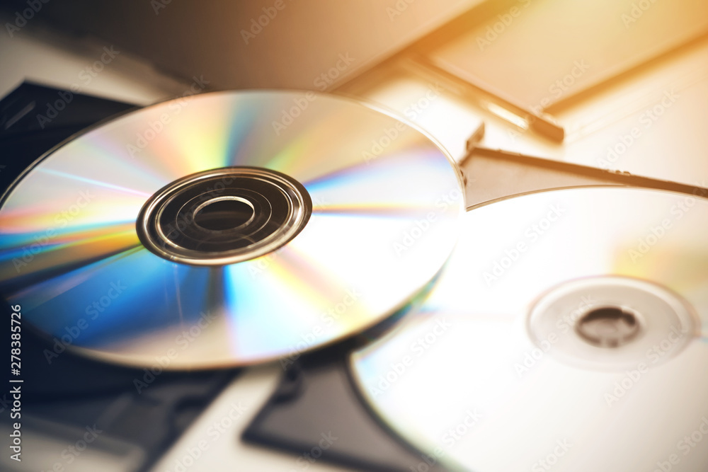 Several CDs lie on a white table in their black boxes, illuminated by sunlight and shimmering with different colors. Several CDs lie on a white table in their black boxes, illuminated by sunlight and shimmering with different colors.