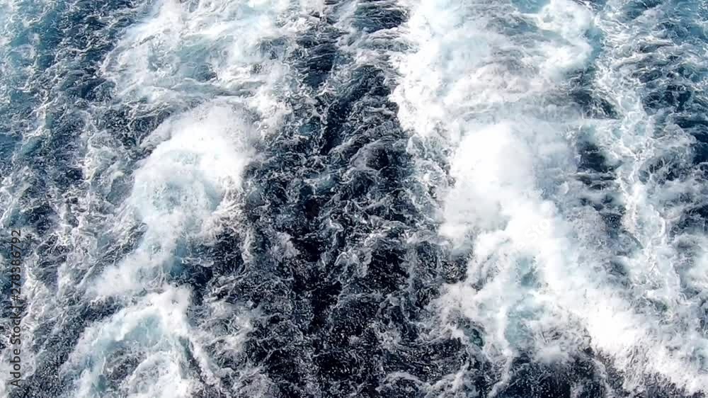 Turbulence in the water behind a large ship, traveling at sea with blue water. Camera fixed.