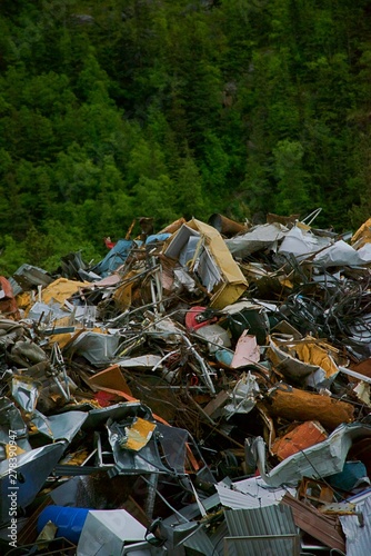 Large junk pile outside of town with trees and hilly background