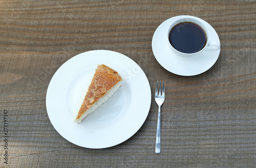 Close up high angle shot of a piece of classic traditional German bee sting cake (Bienenstich), sweet yeast dough with vanilla custard, buttercream and caramelized almond.  A cup of black coffee. 