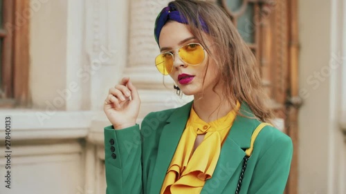 Street fashion portrait of young beautiful elegant lady wearing trendy yellow color sunglasses, headband, stylish blouse, green blazer, posing in old european city photo