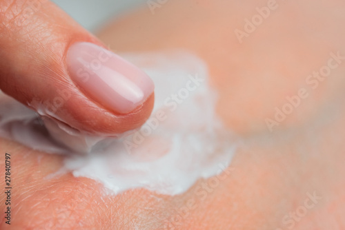 Fingers apply cream to skin. Close up