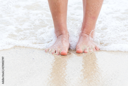 Woman bare foot walking on the summer beach. close up leg of young woman walking along wave of sea water and sand on the beach. Enjoyment barefoot walk outdoor with freedom. Relaxation Travel Concept.